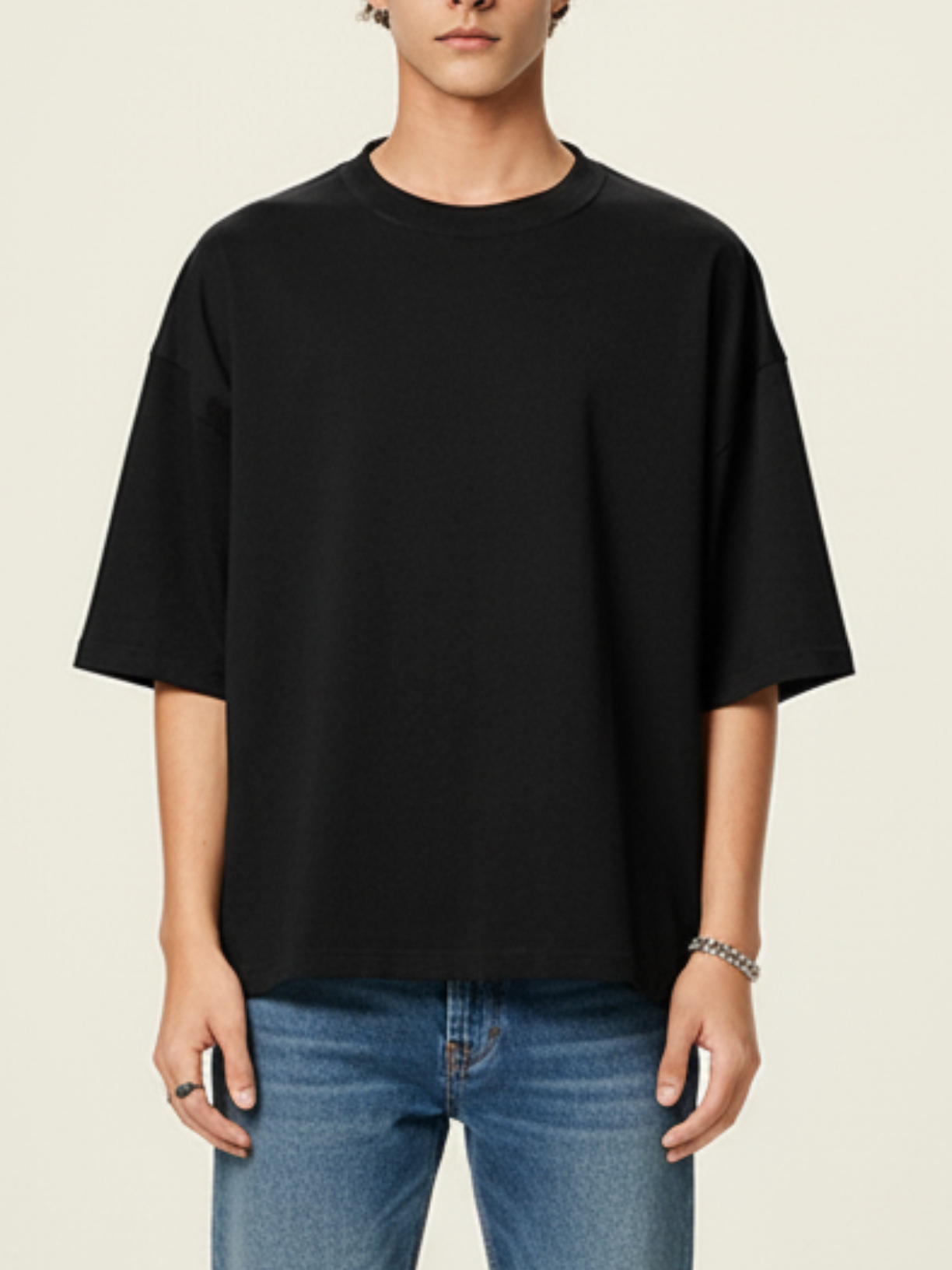 Person wearing a black oversized t-shirt and blue jeans on a beige background