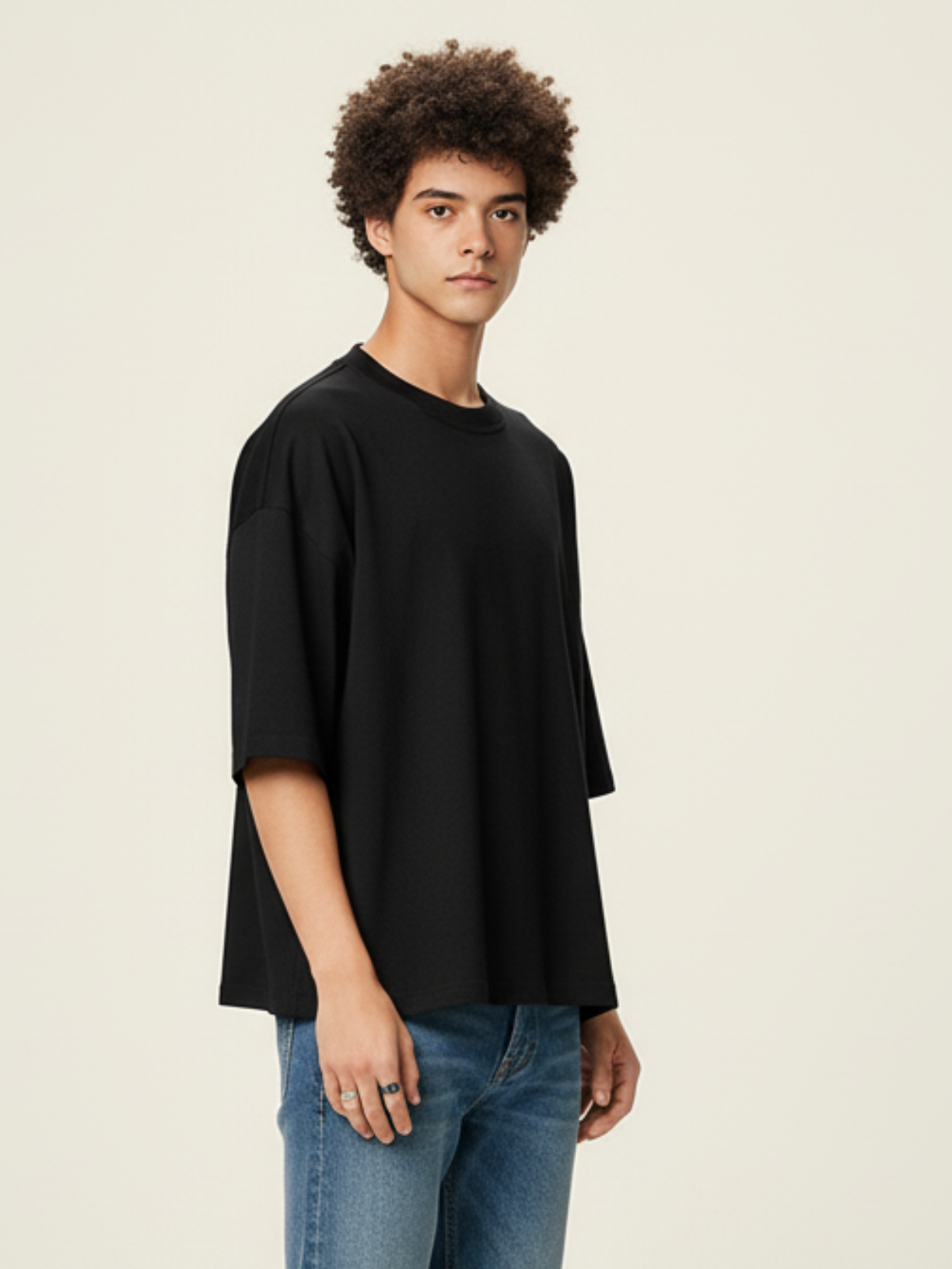 Person wearing a black oversized t-shirt and blue jeans on a beige background