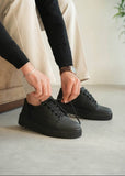 Person tying black sneakers on a neutral background